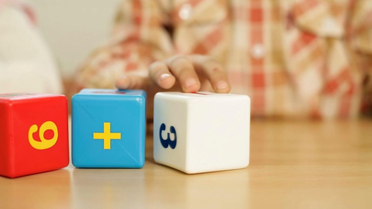 A child's hand resting on large toy number blocks on a wooden table
