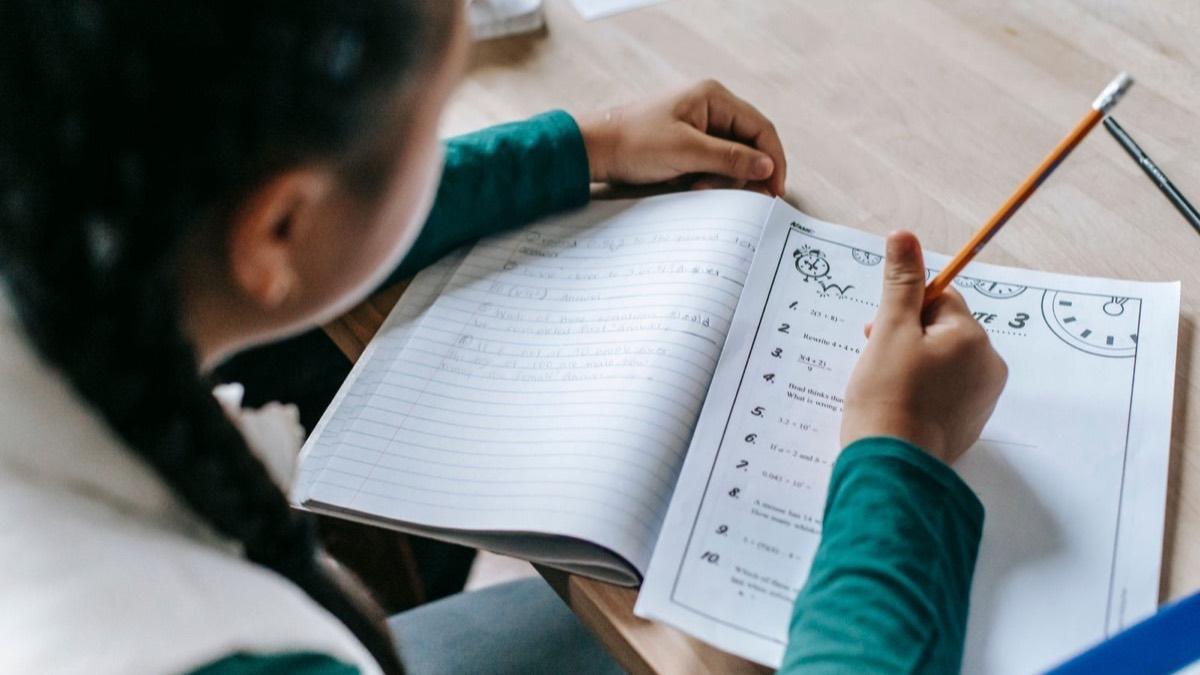 A child working through a math workbook with a pencil, seen from behind