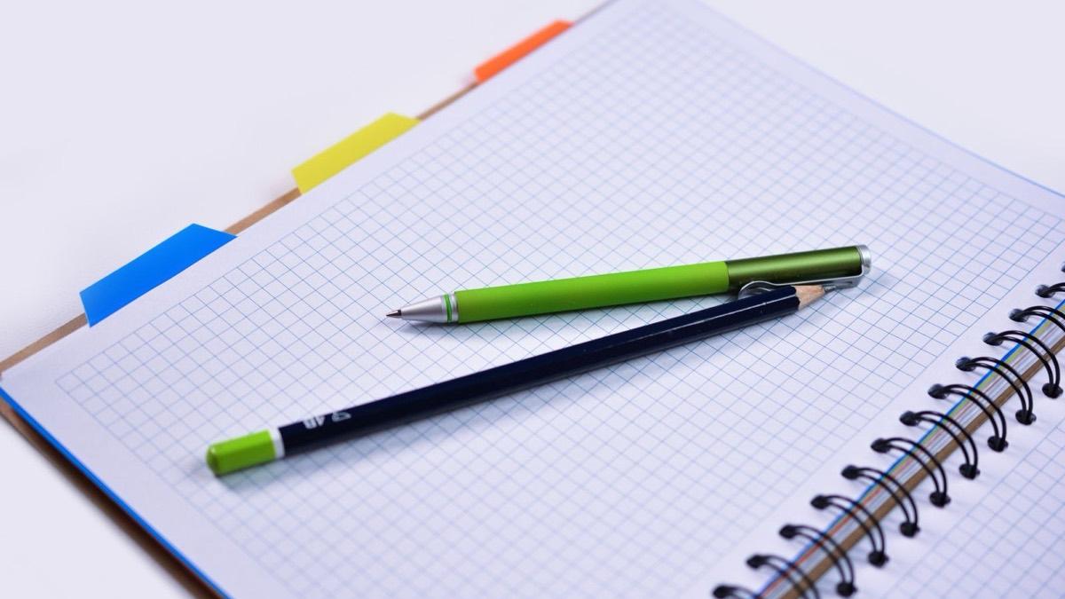 A pencil and a pen resting on a page of graph paper in a spiral notebook