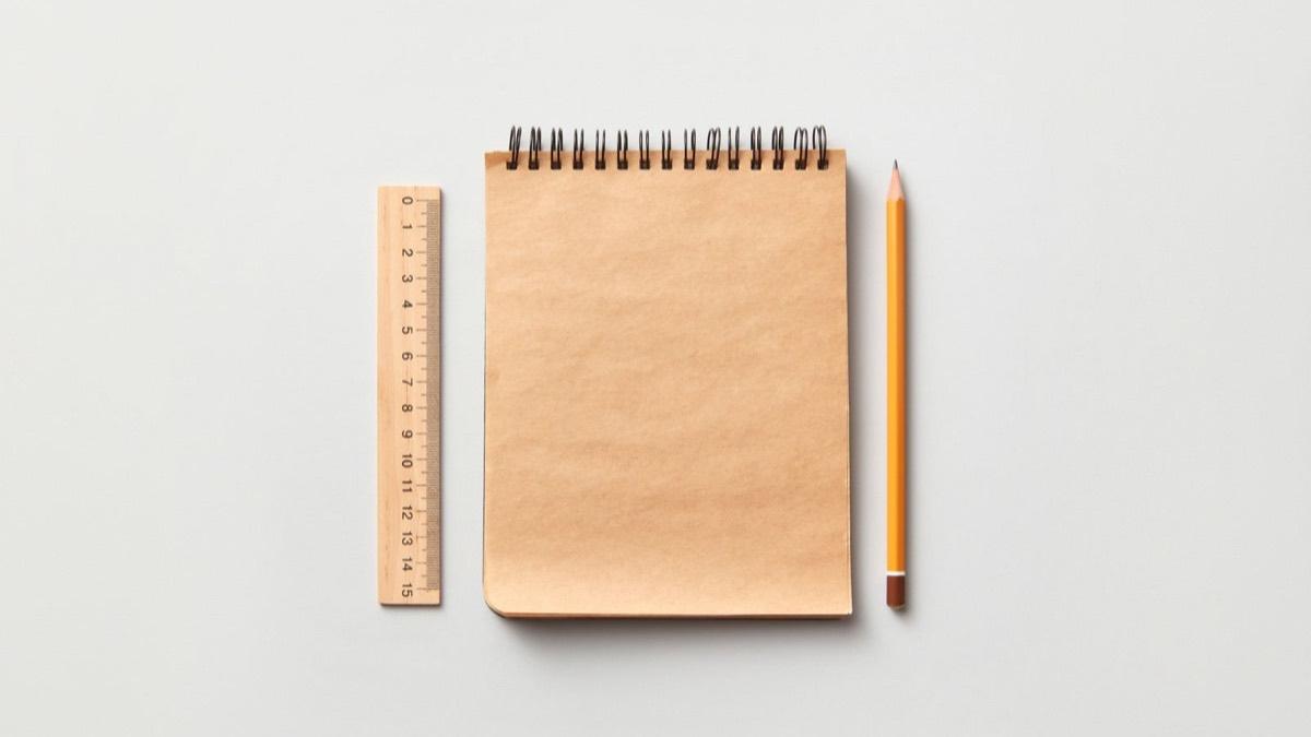 A wooden ruler with centimetre marks beside a notebook and a pencil