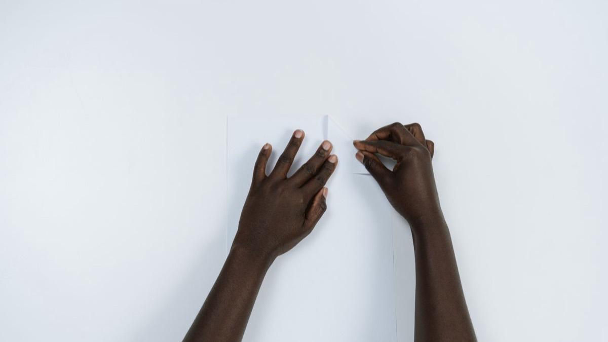 Two hands folding a sheet of white paper on a table